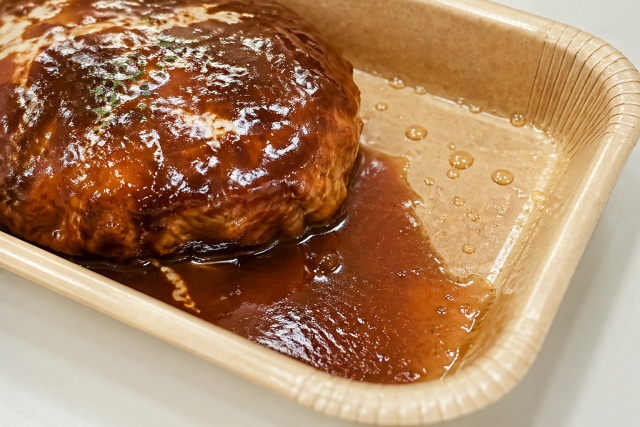 タレだくのハンバーグが盛られたナチュラルペーパートレー。内面PP加工により、ソースが紙に染み込まずに弾かれている様子。