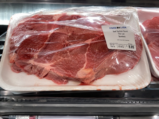 安価な紙トレーから赤いドリップがにじみ、ラップが浮いている精肉のパッケージ