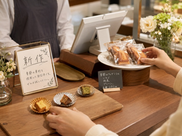レジ横の試食を手に取り、新商品を購入しようとするお客様の手元