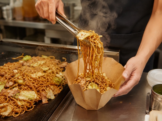 熱い焼きそばを容器に盛り付けている様子