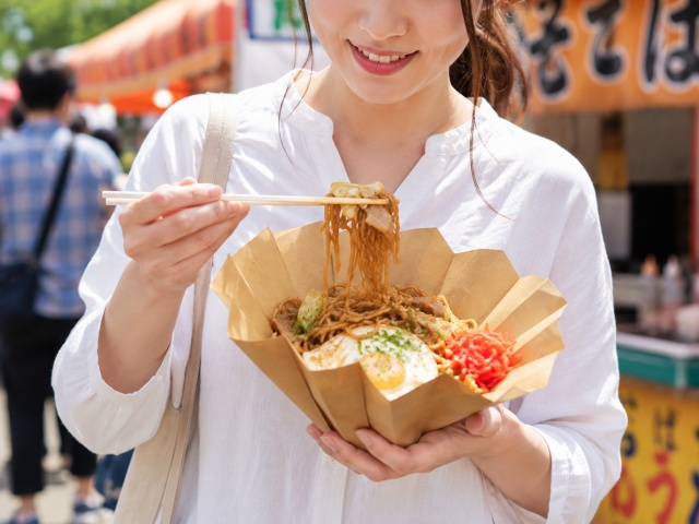 片手で容器を持ち、箸で焼きそばを食べている様子