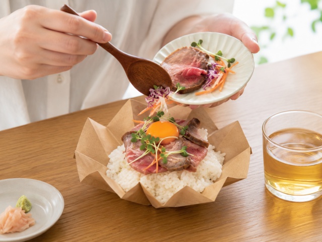 おりがみカップの丼ものを別容器の具材で仕上げている様子
